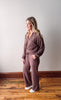 Woman wearing a brown outfit standing on a wooden floor against a white wall