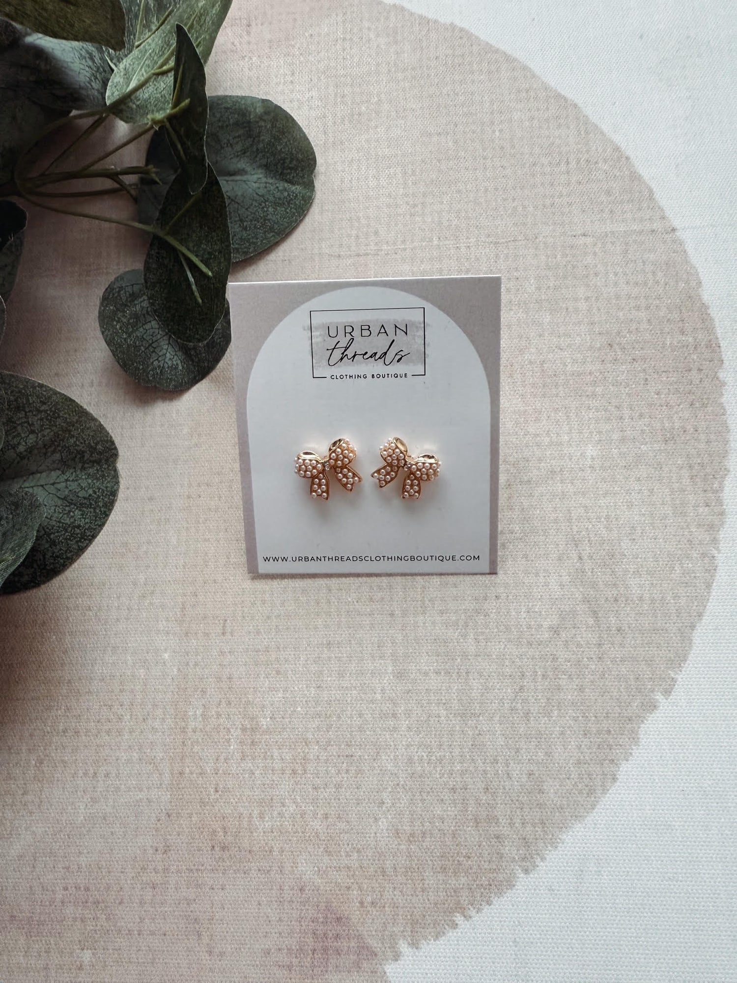 Rose gold earrings on a 'Urban Threads' branded card with green leaves in the background