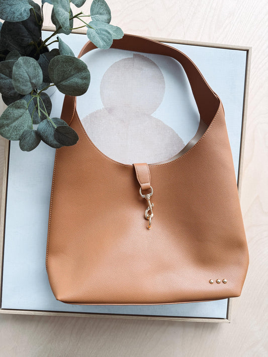 Brown leather handbag on a light surface with a plant in the corner
