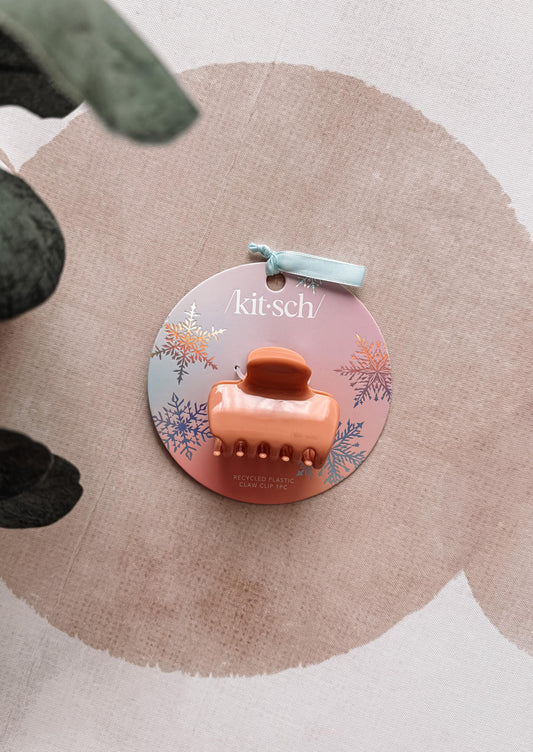 Orange hair clip on a 'kit-sch' branded card with a floral design on a beige background