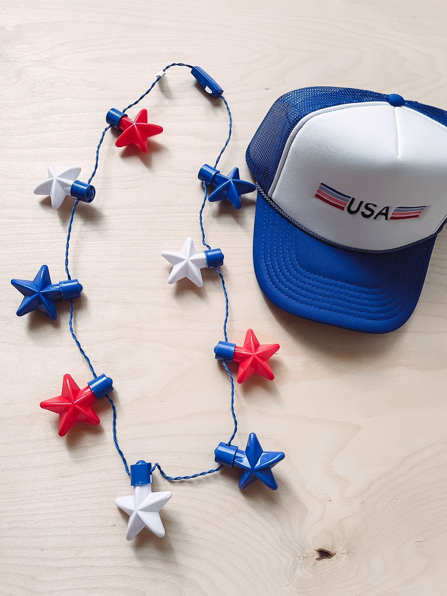 A necklace with red, white, and blue stars and a blue hat with 'USA' and 'Texas' text on it, placed on a wooden surface.