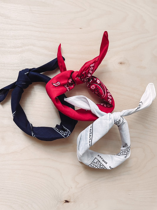 Three triangular bandanas, two red and one white, with a patterned design, displayed on a wooden surface.