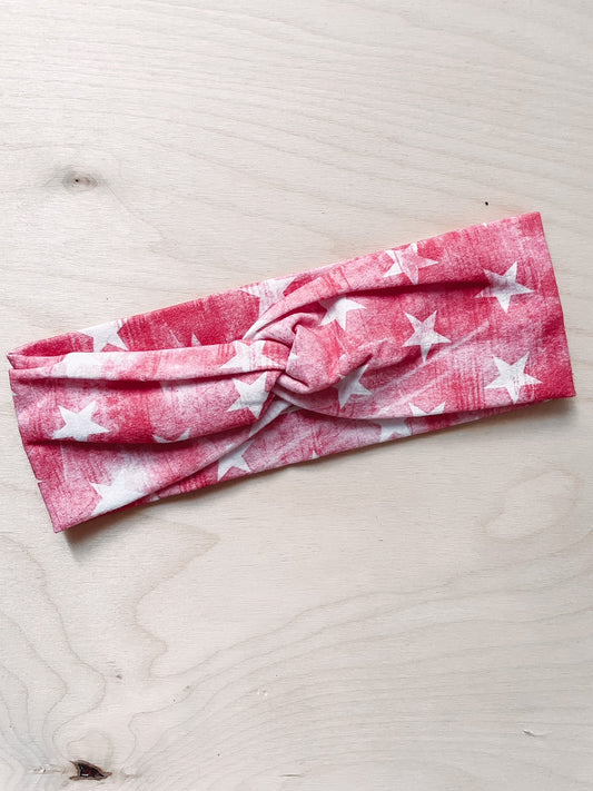 A red headband with white stars pattern, laid flat on a wooden surface.