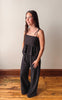 Woman wearing a black polka dot jumpsuit standing on a wooden floor against a plain wall.