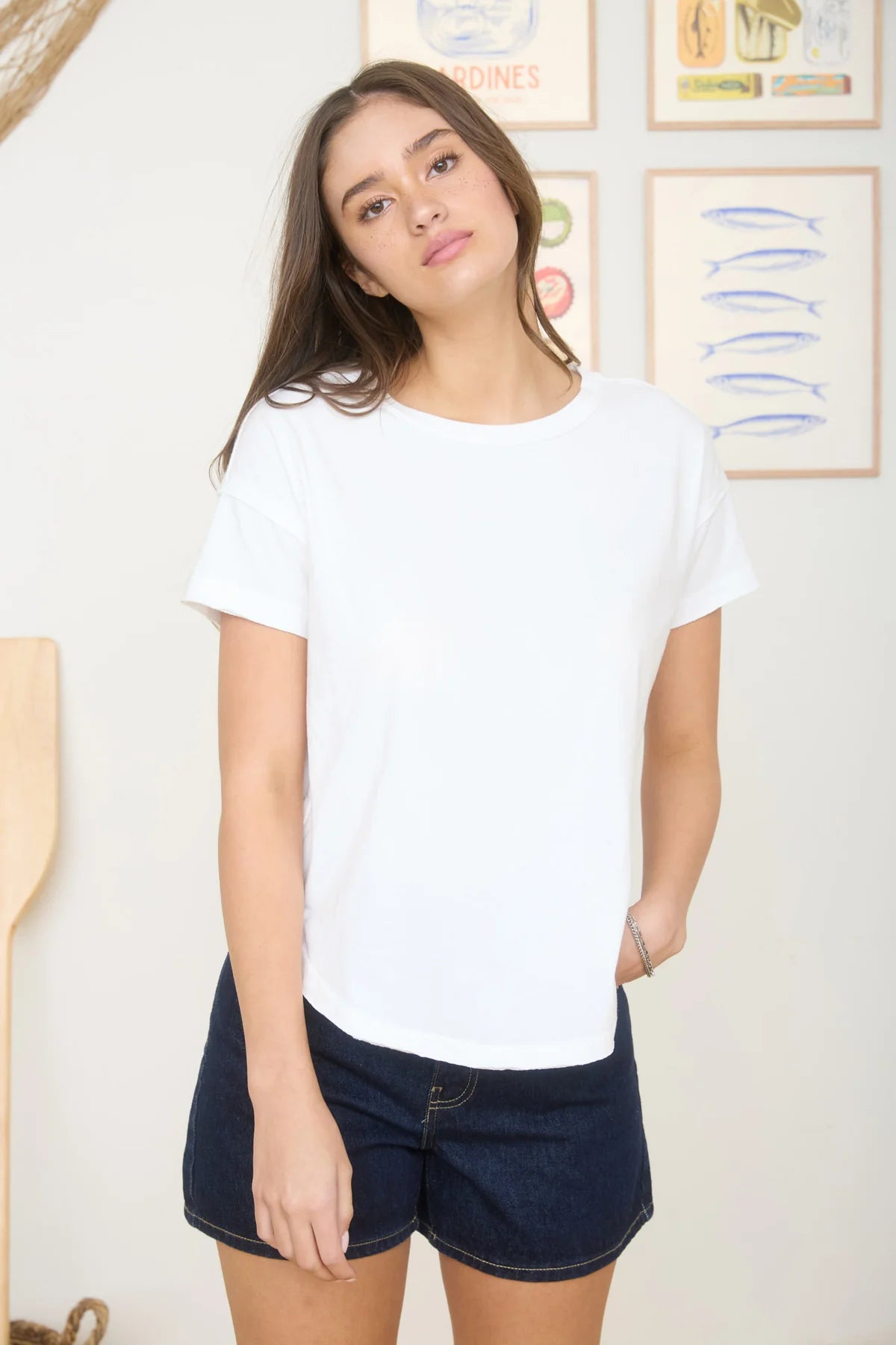 Woman wearing a white t-shirt and dark shorts indoors with a neutral background