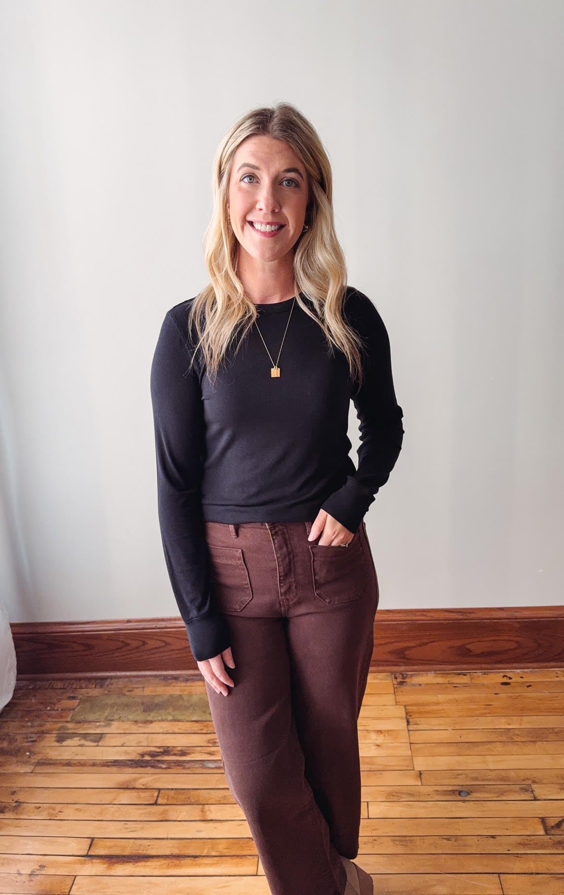 Woman wearing a black sweater and brown pants standing on a wooden floor.