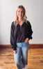 Woman wearing a dark gray sweatshirt with a zipper and light blue jeans standing on a wooden floor.
