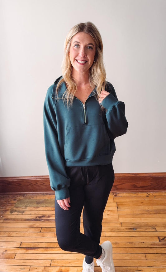 Woman wearing a teal sweatshirt and black pants on a wooden floor.