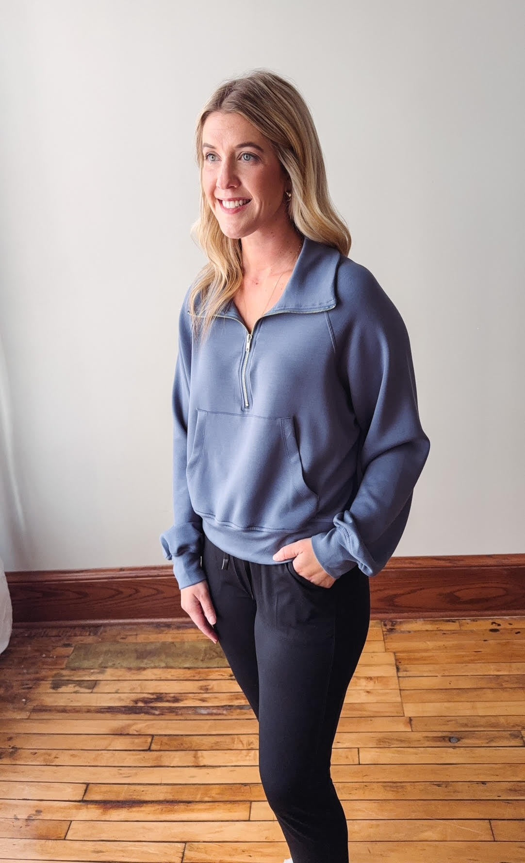 Woman wearing a blue pullover with a quarter zip in a room with wooden flooring.