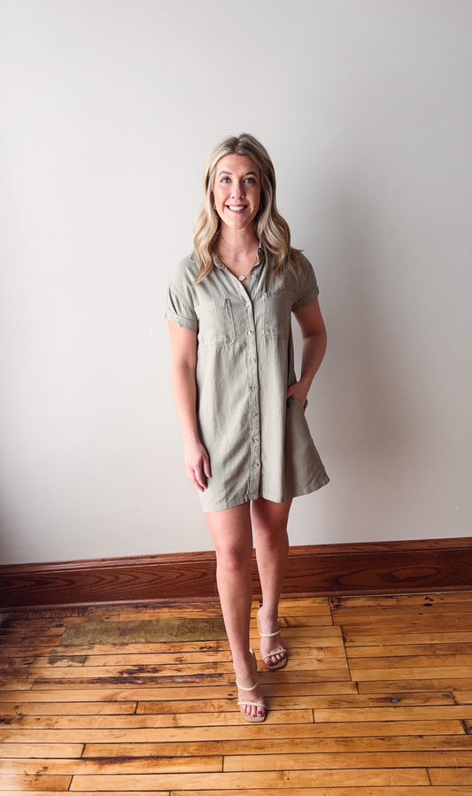 Woman wearing a green dress standing on a wooden floor with a white wall background