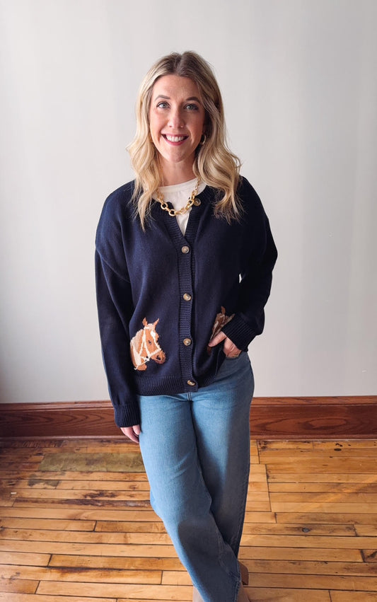 Woman wearing a navy blue cardigan and light blue jeans standing on a wooden floor.