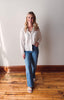 Woman wearing a white blouse and blue jeans standing on a wooden floor with a white wall background