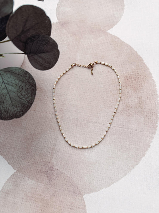 Delicate necklace on a textured surface with leaves in the background