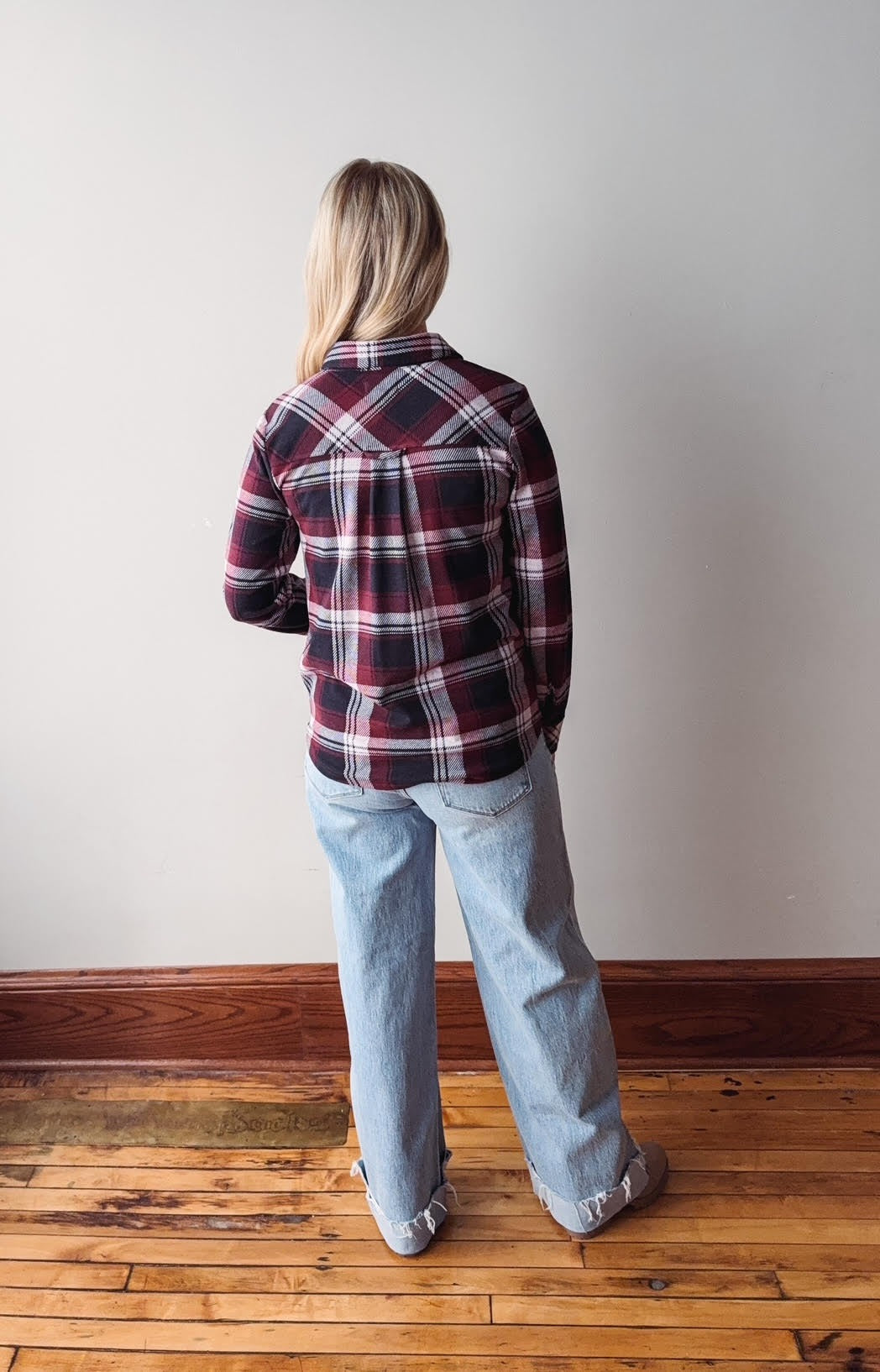 Person wearing a plaid shirt and jeans standing against a plain wall.