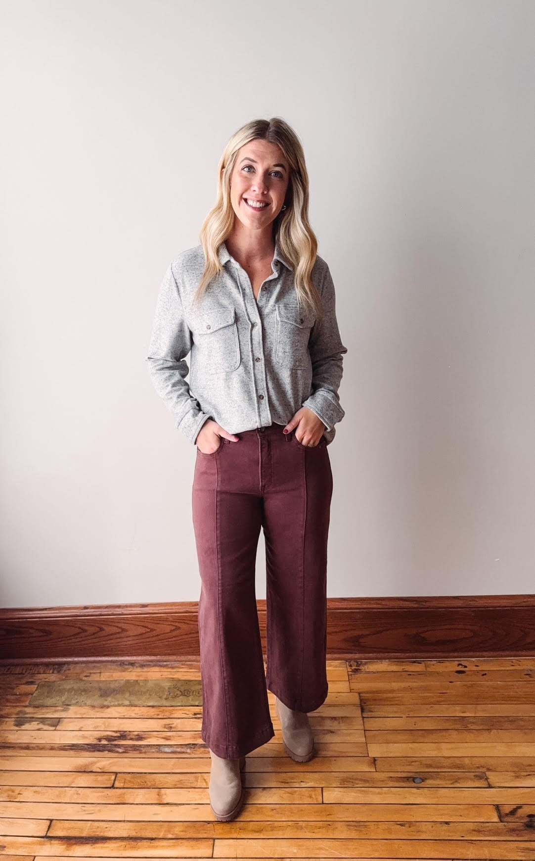 Woman wearing a light gray shirt and maroon pants standing on a wooden floor.