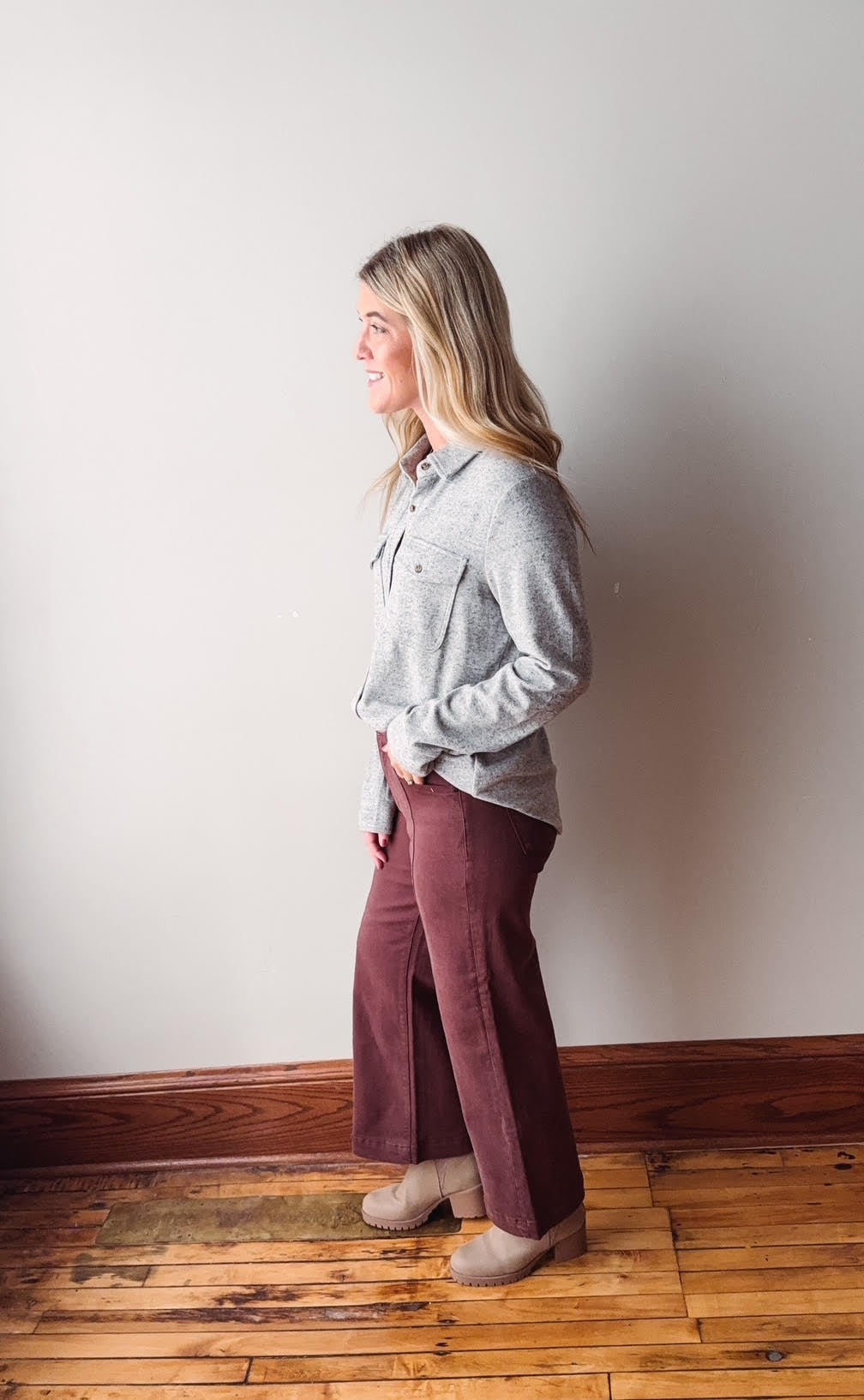 Person wearing a gray shirt and maroon pants standing against a white wall.