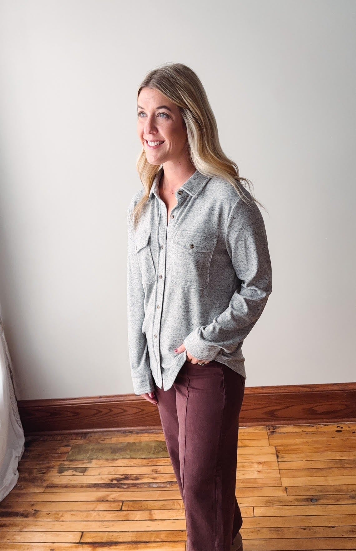 Woman wearing a gray shirt and maroon pants standing against a white wall.