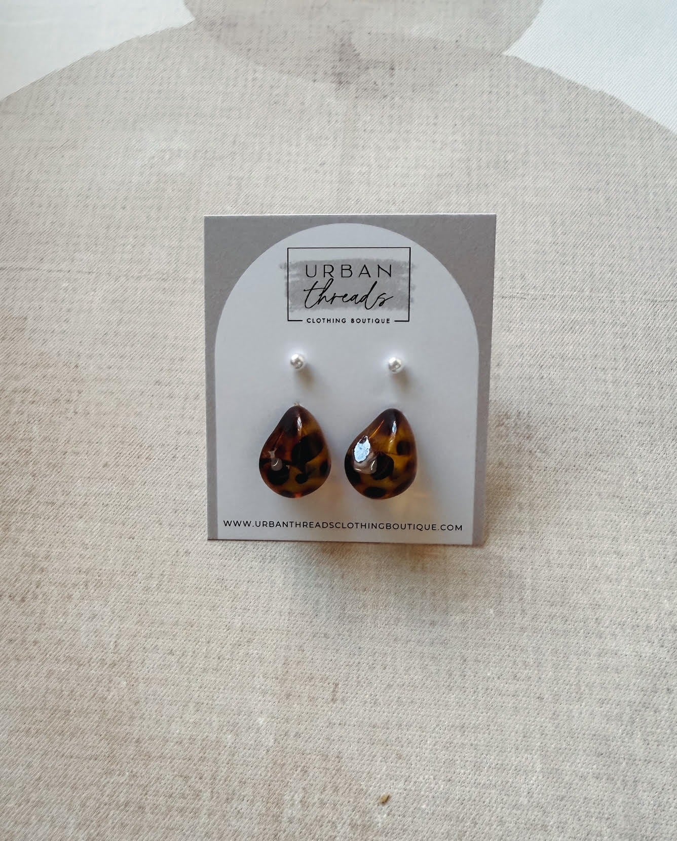 Teardrop-shaped tortoiseshell earrings on a 'Urban Threads' branded card against a beige background.