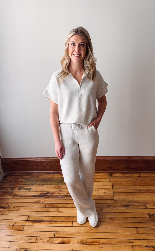 Woman wearing a white outfit standing on a wooden floor with a plain white wall background