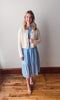 Woman wearing a light blue dress with a white cardigan in a room with wooden flooring.