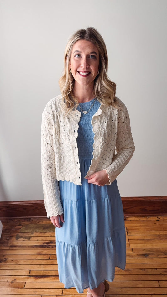 Woman wearing a light blue dress with a cream cardigan against a plain background