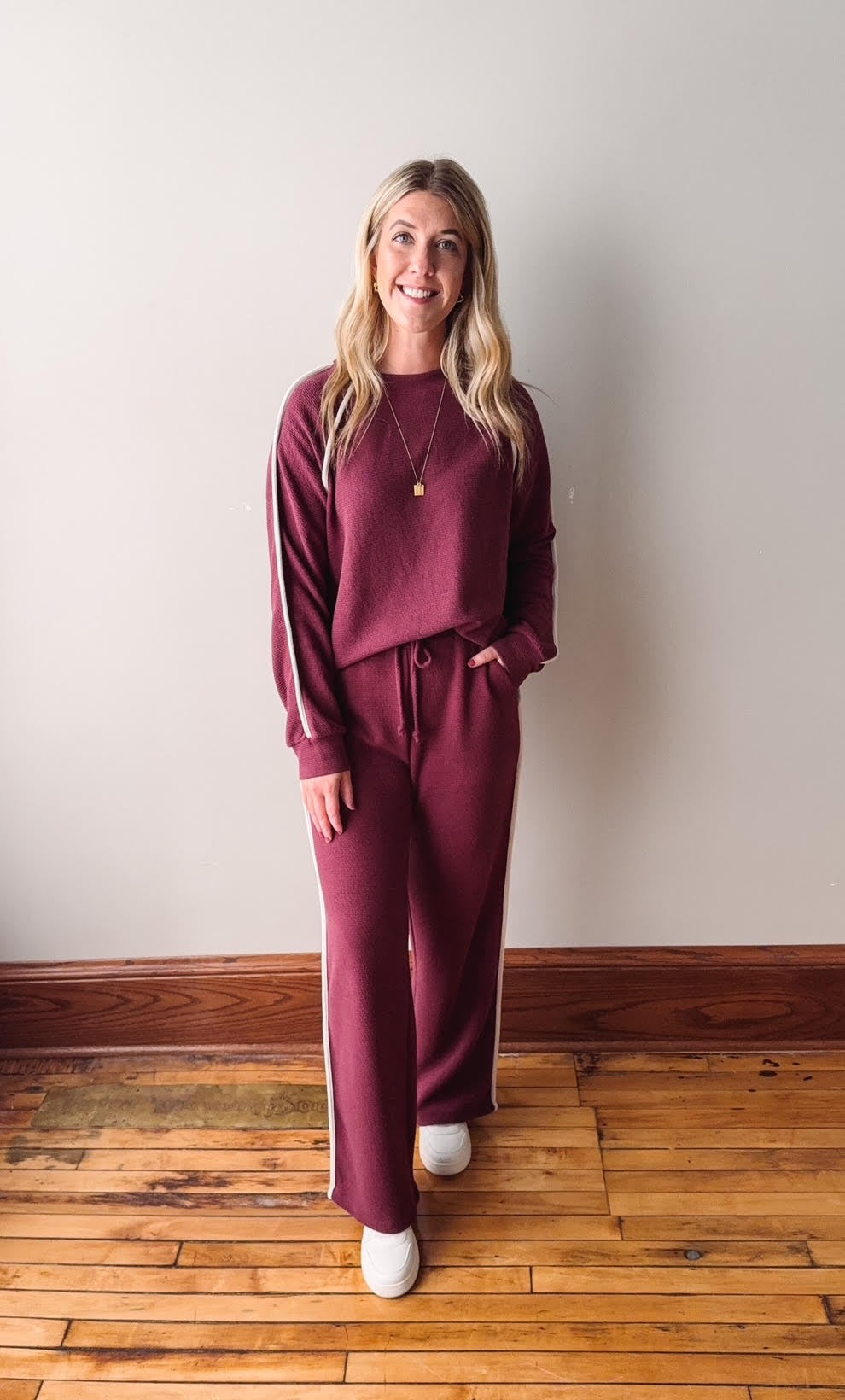Woman wearing a burgundy outfit standing on a wooden floor against a white wall