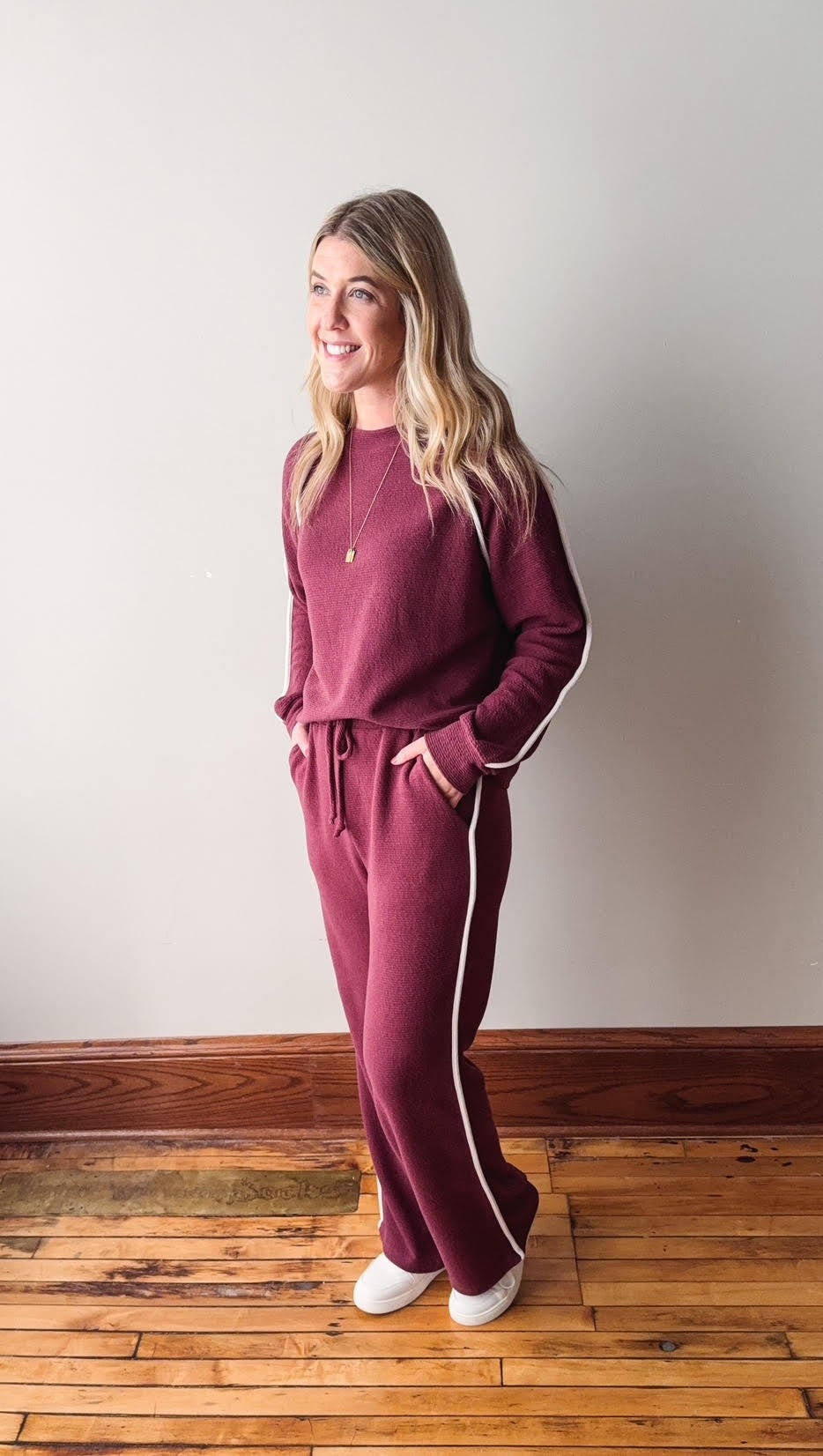 Woman wearing a maroon tracksuit with white stripes on a wooden floor.