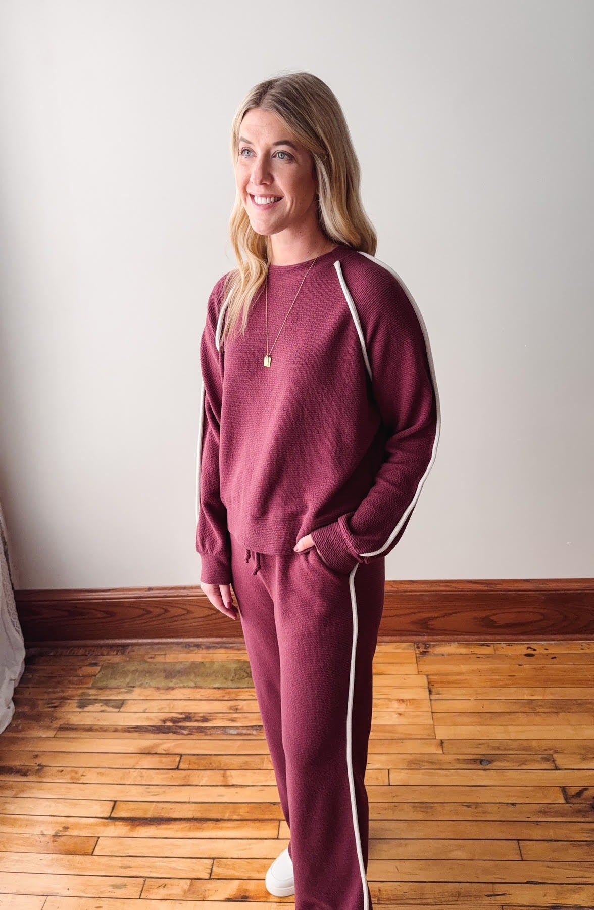 Woman wearing a maroon tracksuit with white stripes on a wooden floor.