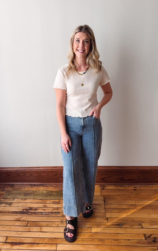 Woman wearing a white t-shirt and blue jeans standing on a wooden floor with a white wall background