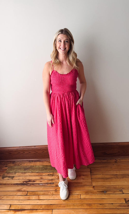 Woman wearing a pink dress standing on a wooden floor against a white wall
