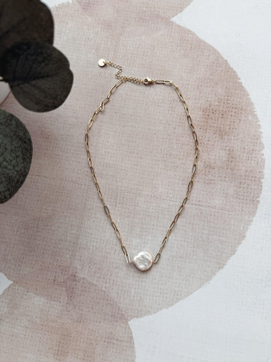 Gold chain necklace with a pearl pendant on a textured surface