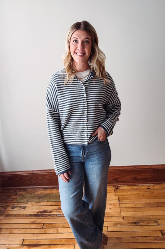 Woman wearing a striped shirt and jeans standing on a wooden floor with a white wall background