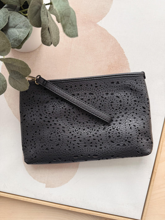 Black textured clutch bag on a light background with a plant