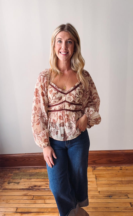 Woman wearing a floral blouse and blue jeans standing in a room with wooden flooring.