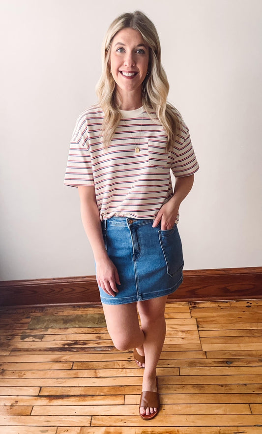 A woman wearing a red and white striped pocket tee with a blue denim skirt and beige sandals.