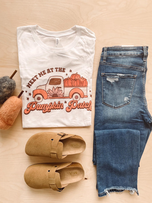 A white graphic tee with the text 'Pumpkin Patch' and an illustration of a retro pumpkin truck, paired with blue jeans and brown shoes.
