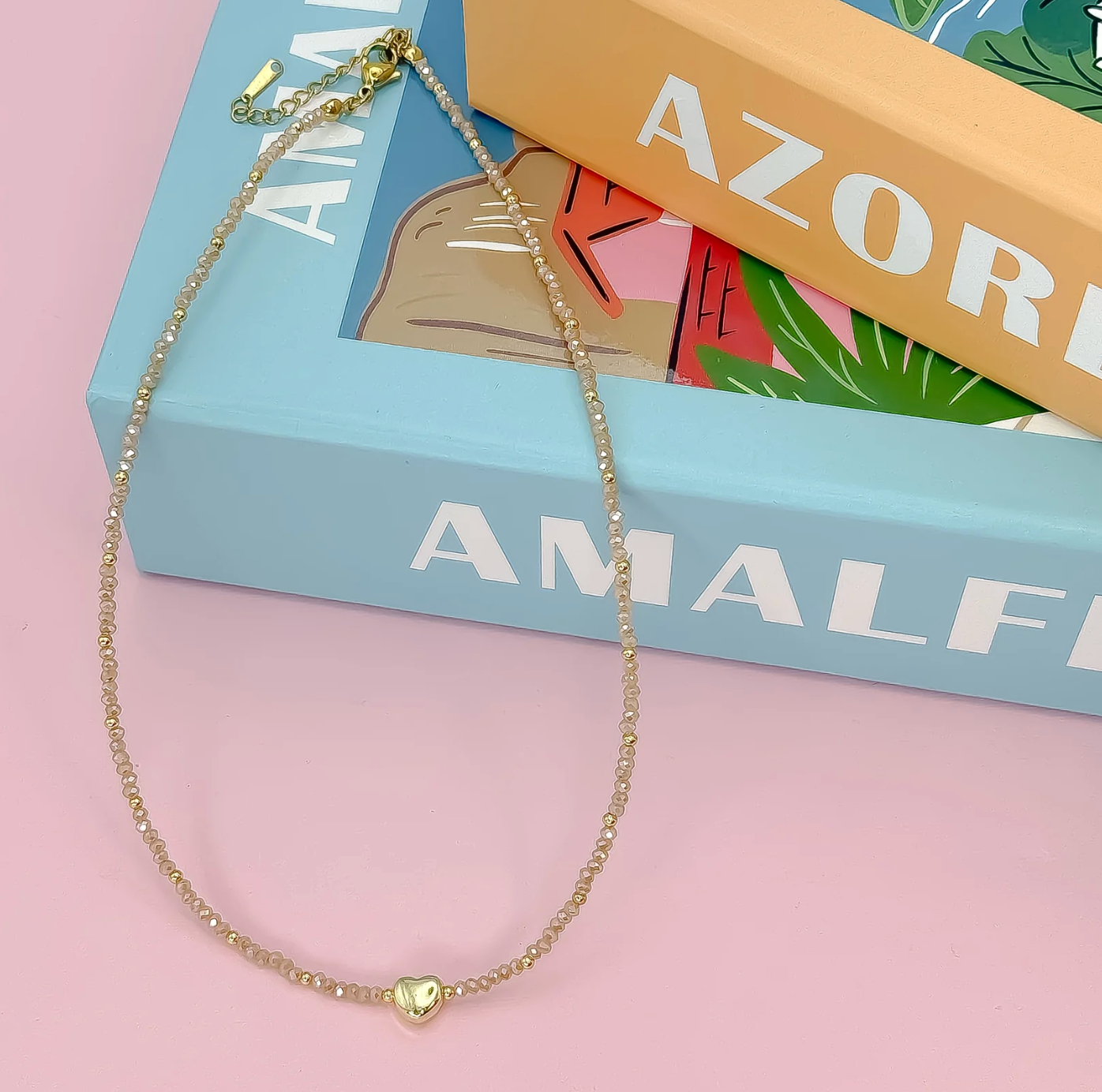 Gold necklace with a heart pendant on a pink surface with books in the background