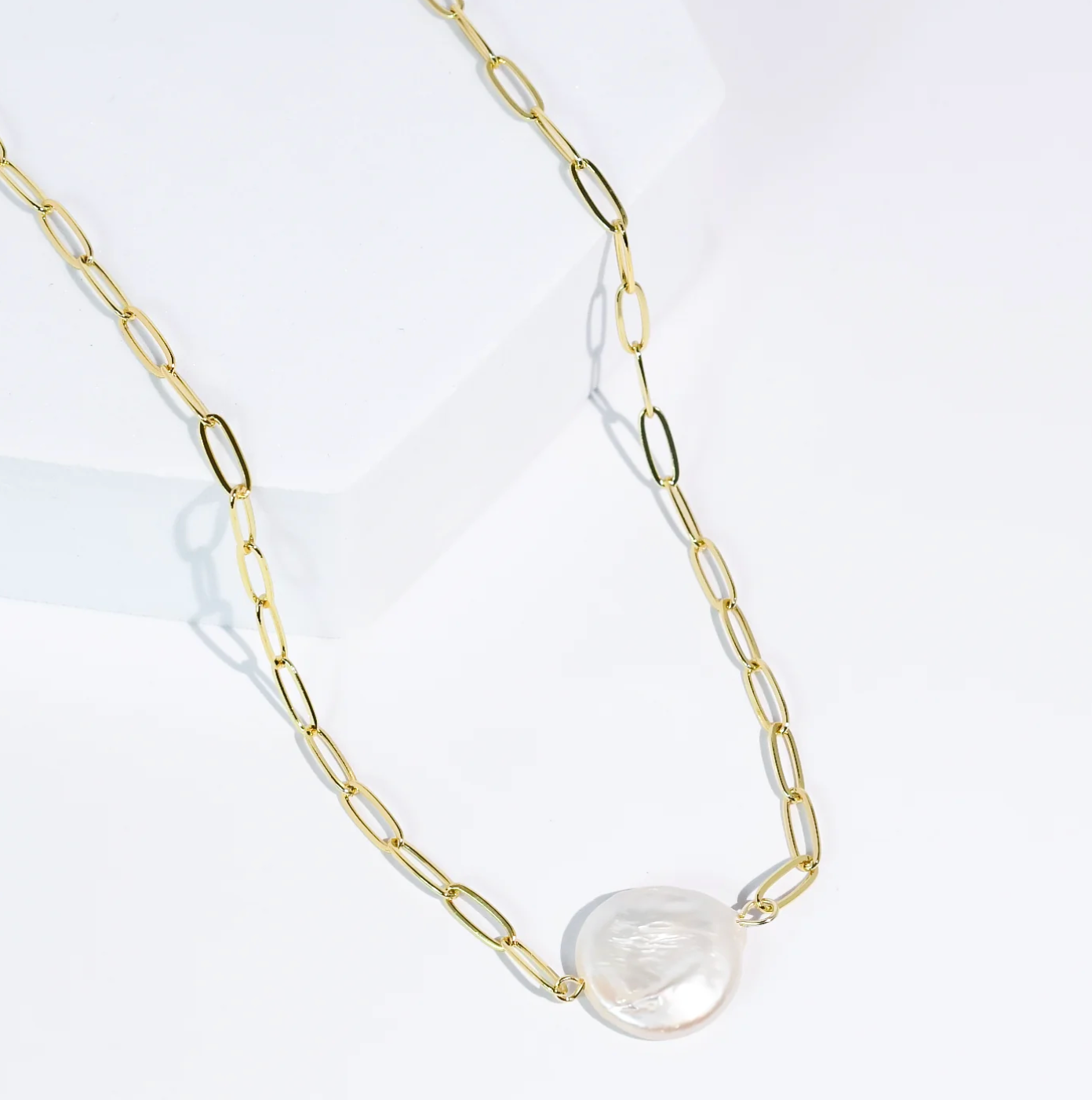 Gold chain necklace with a large pearl pendant on a white background