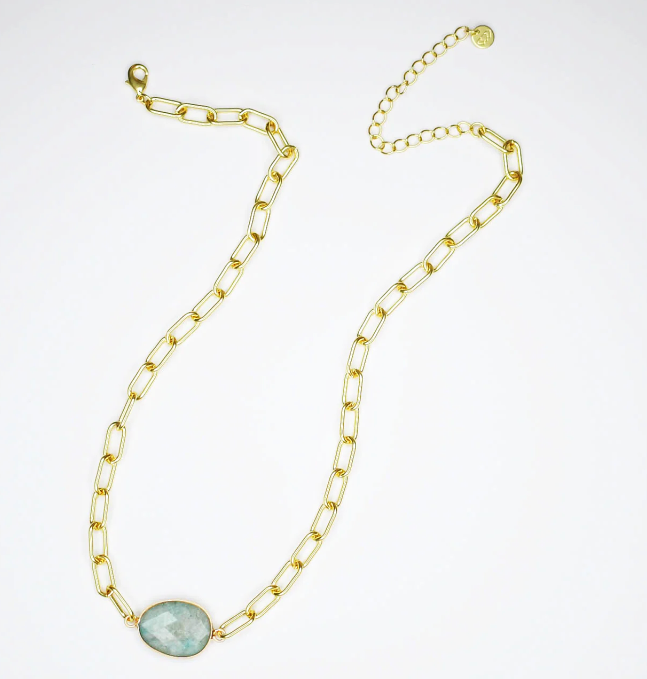 Gold chain necklace with a green gemstone on a white background