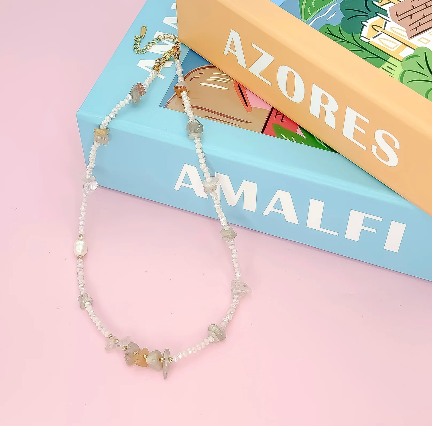 Beaded necklace on a book with 'Azores' and 'Amalfi' text on a pink background