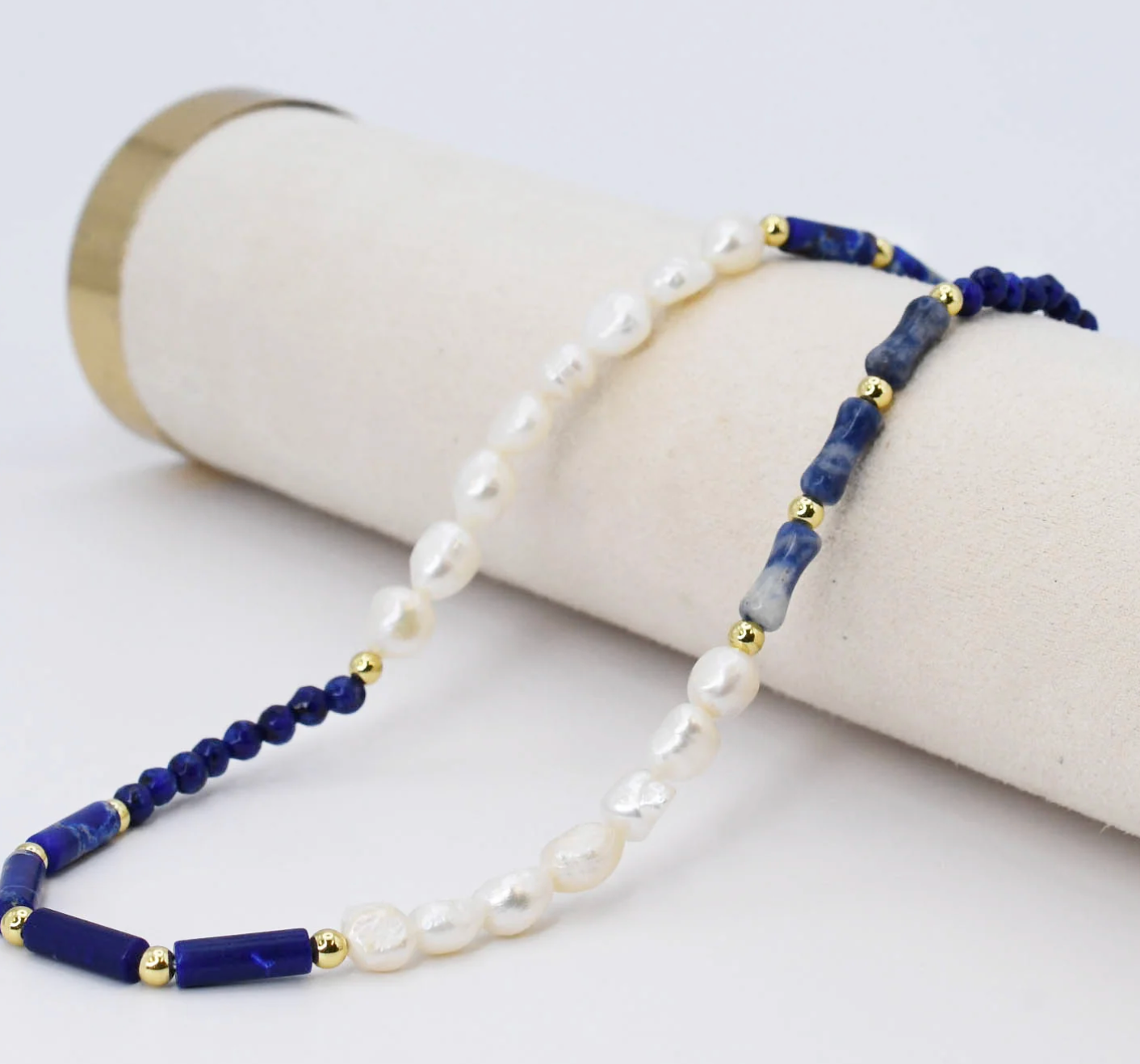 Beaded necklace with blue and white beads on a cylindrical white stand.