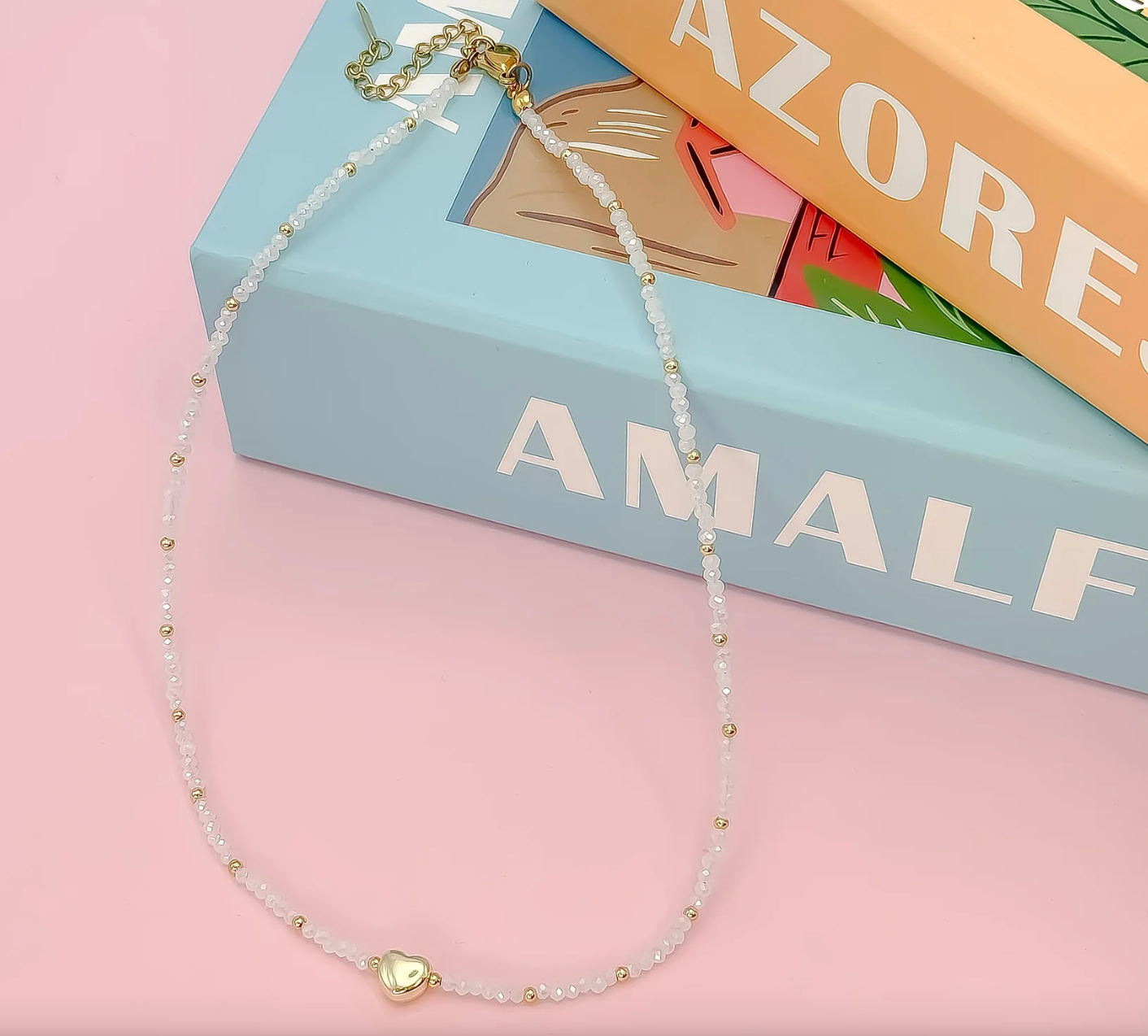 Necklace with a heart-shaped pendant on a pink surface with a book in the background