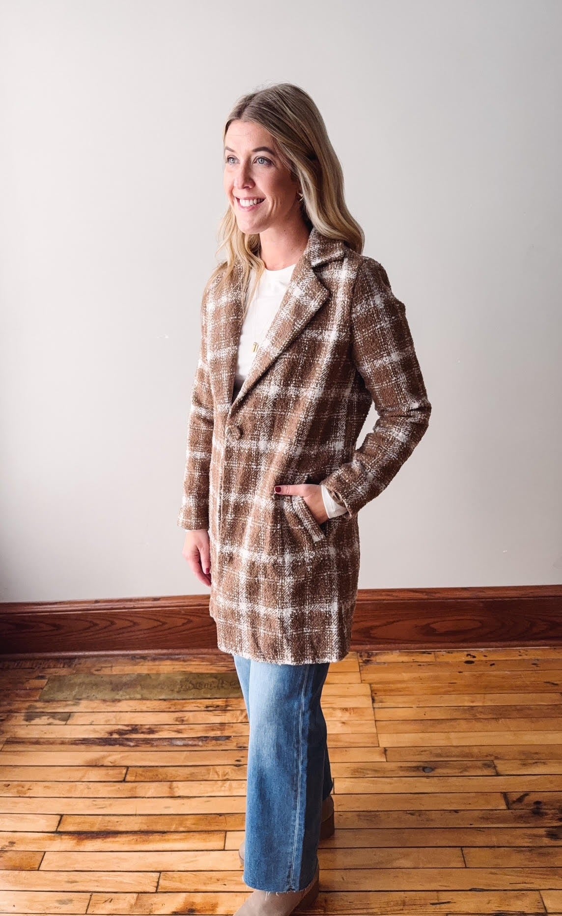 Woman wearing a plaid coat standing on a wooden floor with a white wall background