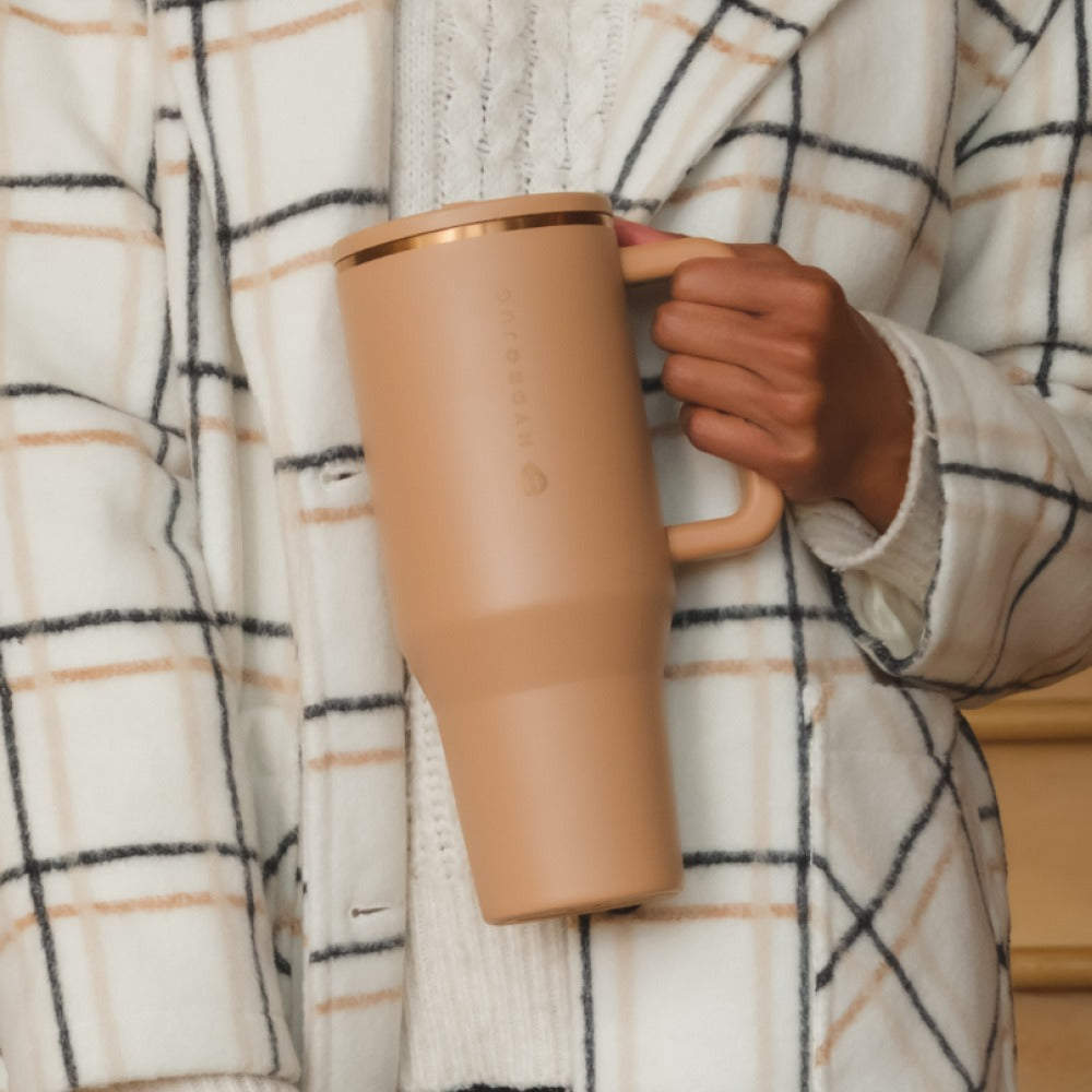 Person holding a brown mug wrapped in a plaid blanket