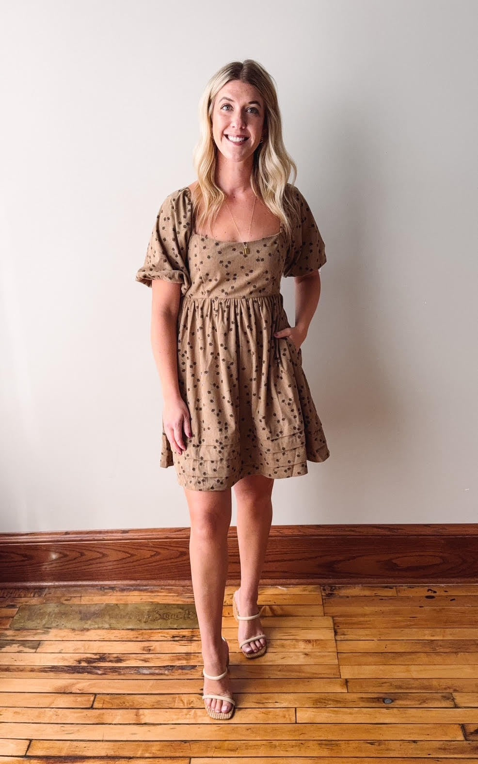 Woman wearing a patterned dress standing on a wooden floor against a white wall