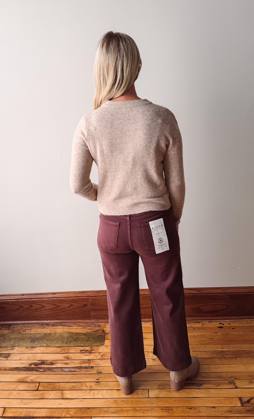 Person wearing a taupe sweater and maroon pants on a wooden floor with a white wall.