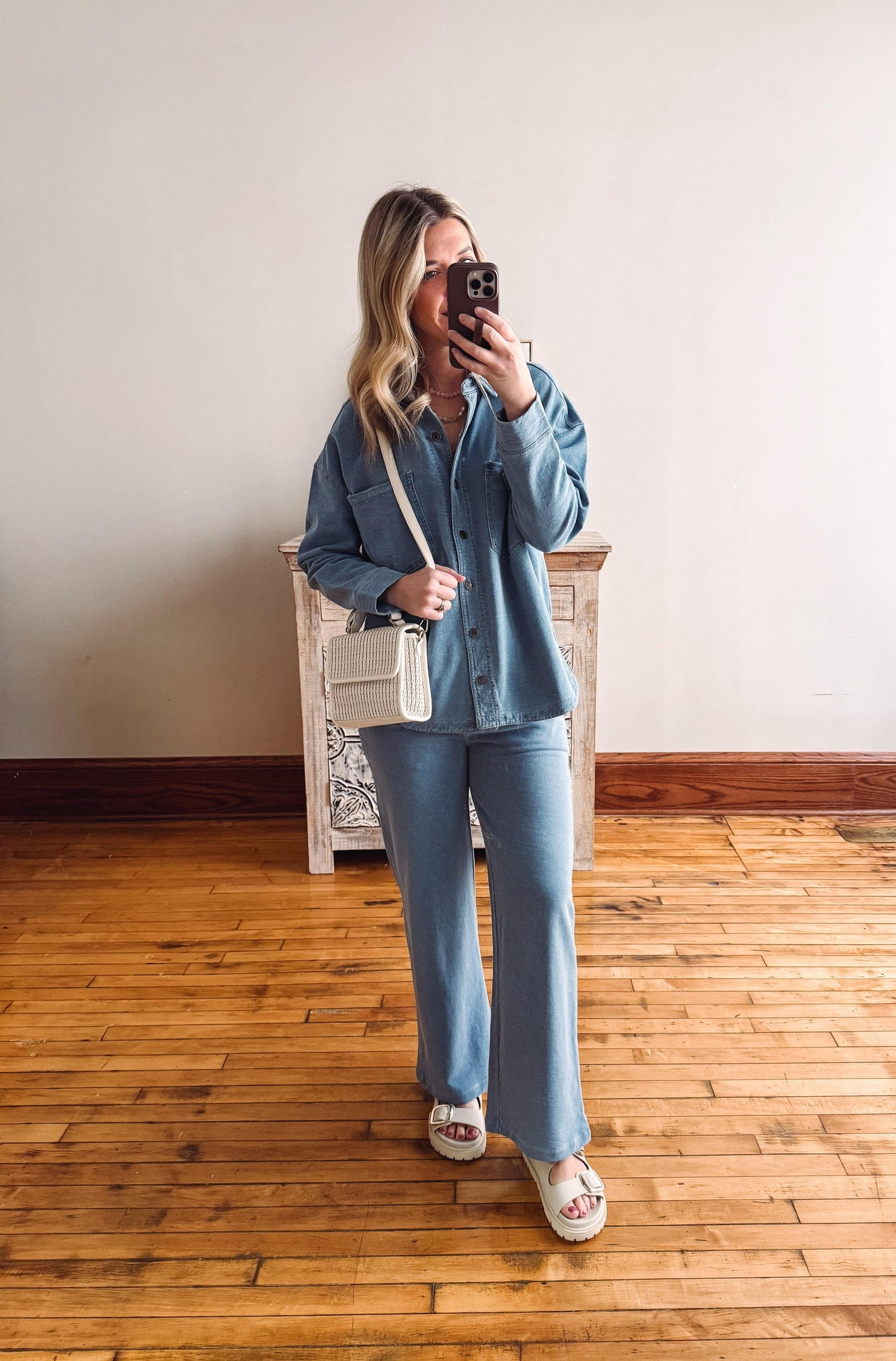 Person taking a mirror selfie wearing a blue outfit with a white handbag.