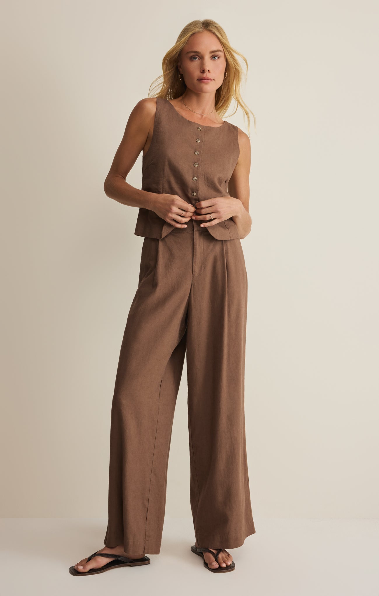 Woman wearing a brown sleeveless top and wide-leg pants on a beige background