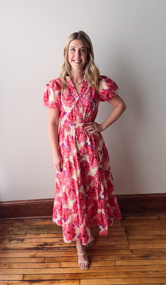 Woman wearing a red floral dress standing on a wooden floor against a white wall.
