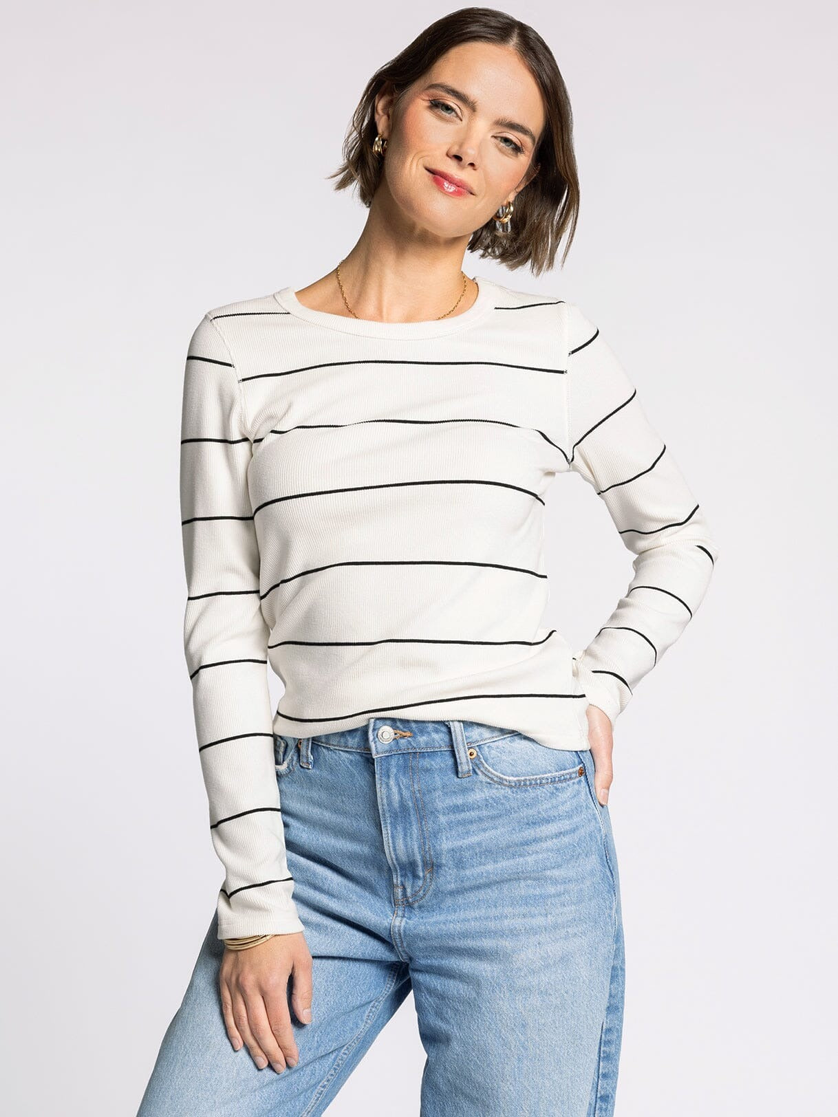 Woman wearing a white sweater with black stripes and blue jeans on a light gray background